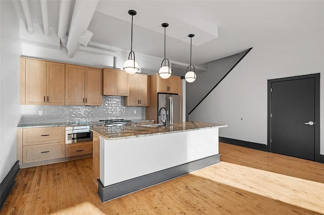 kitchen featuring light stone counters, stainless steel appliances, a sink, light wood-type flooring, and decorative backsplash