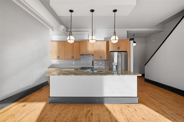 kitchen with decorative backsplash, dark stone counters, a kitchen island with sink, stainless steel refrigerator with ice dispenser, and a sink