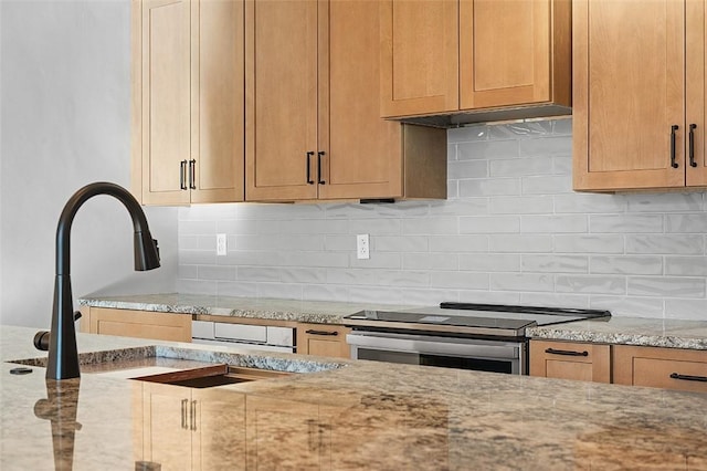 kitchen featuring tasteful backsplash, stainless steel range with electric cooktop, a sink, and light stone countertops