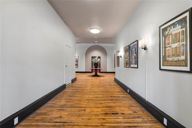 corridor featuring baseboards, arched walkways, and wood finished floors