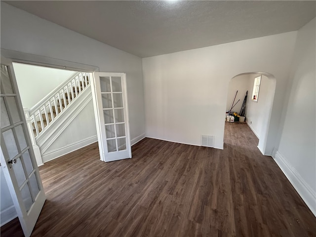 unfurnished room featuring dark wood-style floors, visible vents, stairs, and arched walkways