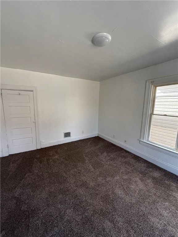 spare room with visible vents, dark carpet, and baseboards