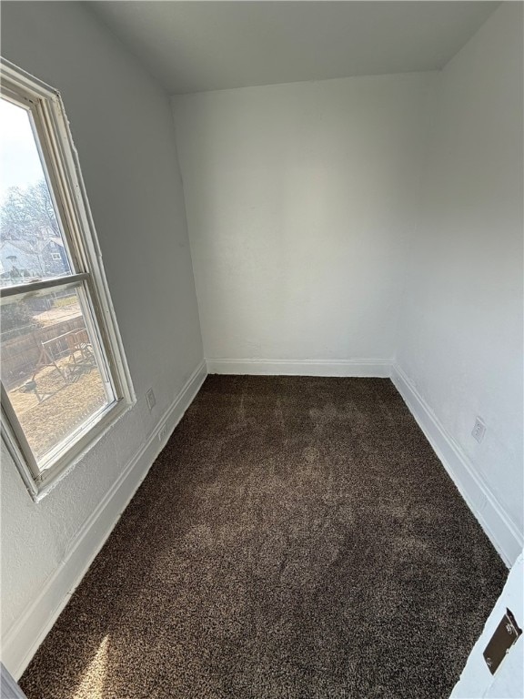 spare room featuring dark carpet and baseboards