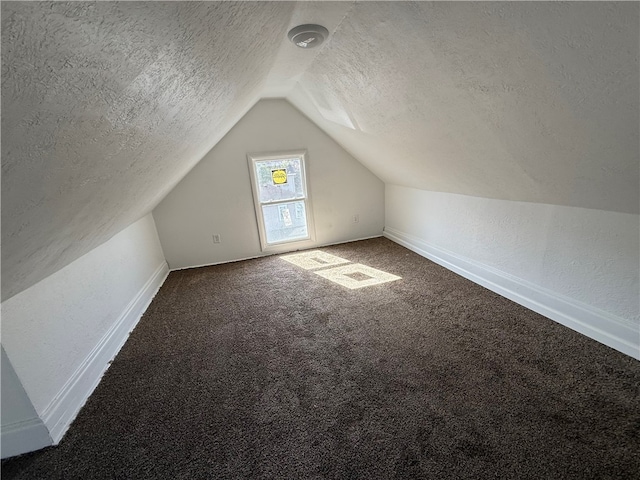 additional living space featuring a textured wall, carpet flooring, vaulted ceiling, a textured ceiling, and baseboards