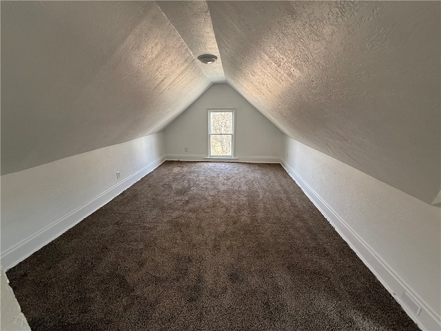 additional living space with lofted ceiling, baseboards, dark carpet, and a textured ceiling