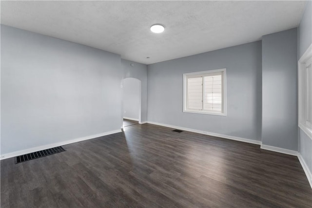 unfurnished room featuring arched walkways, dark wood-style flooring, visible vents, and baseboards