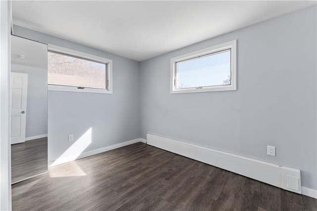 spare room featuring a baseboard heating unit, baseboards, and wood finished floors