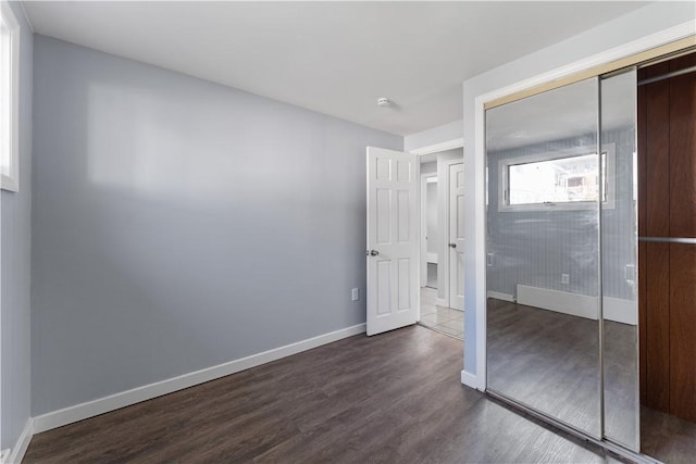 unfurnished bedroom with dark wood-style floors, a closet, and baseboards