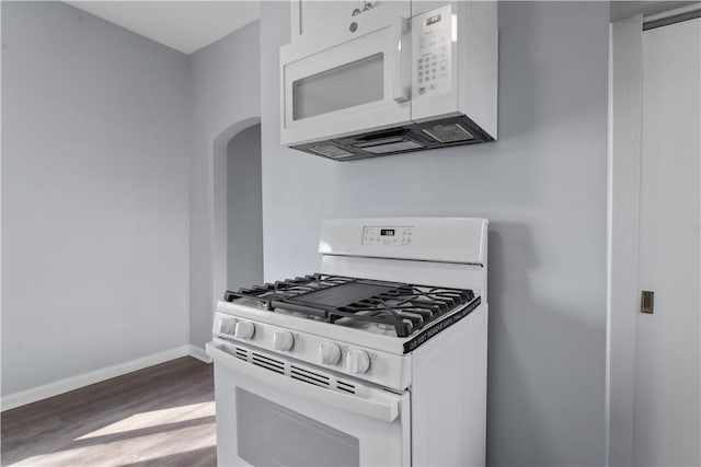 kitchen with white appliances, baseboards, arched walkways, wood finished floors, and white cabinetry