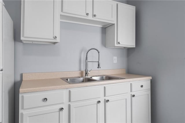 kitchen with light countertops, a sink, freestanding refrigerator, and white cabinets