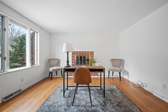 office space featuring baseboards, visible vents, wood finished floors, and a glass covered fireplace