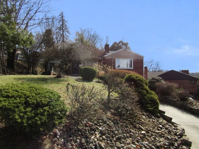 exterior space featuring brick siding, a chimney, and a front lawn