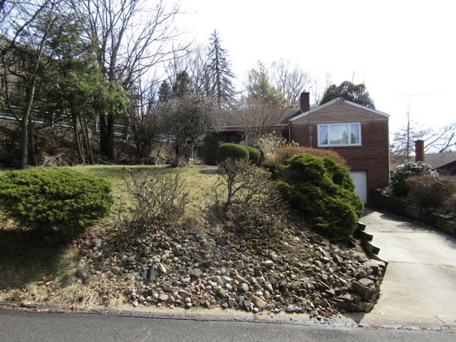 view of front facade featuring concrete driveway, brick siding, a chimney, and an attached garage