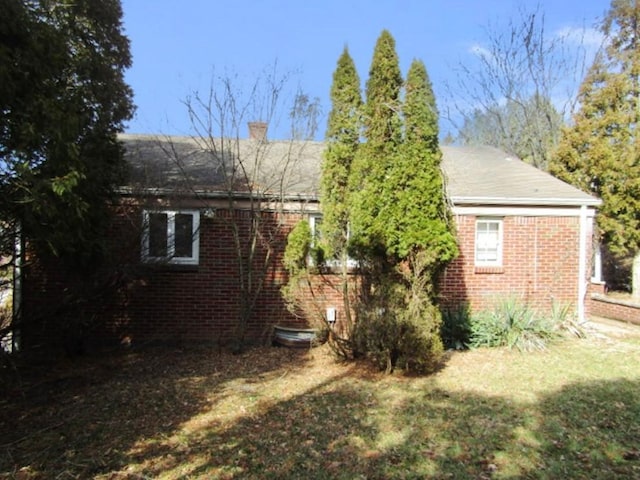 exterior space featuring brick siding, a chimney, and a lawn