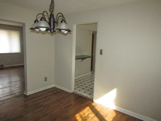 unfurnished dining area featuring visible vents, a notable chandelier, baseboards, and wood finished floors