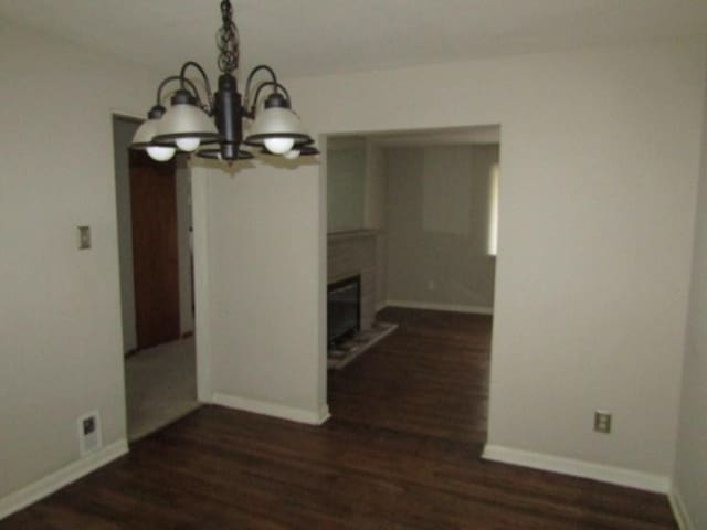 unfurnished dining area with a notable chandelier, baseboards, dark wood-type flooring, and a glass covered fireplace