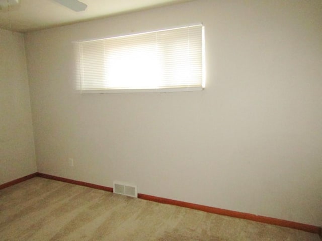 spare room featuring baseboards, visible vents, a ceiling fan, and light colored carpet