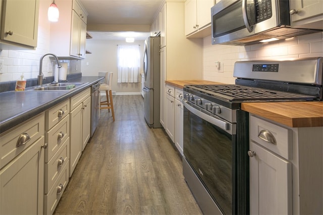 kitchen featuring dark wood finished floors, butcher block countertops, backsplash, stainless steel appliances, and a sink