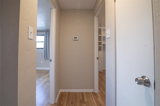 corridor featuring a textured wall, baseboards, and wood finished floors