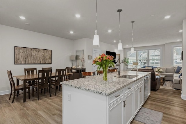 kitchen with an island with sink, light wood-style flooring, open floor plan, white cabinetry, and a sink