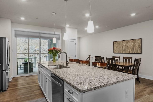 kitchen with stainless steel appliances, a sink, light stone countertops, dark wood finished floors, and a center island with sink