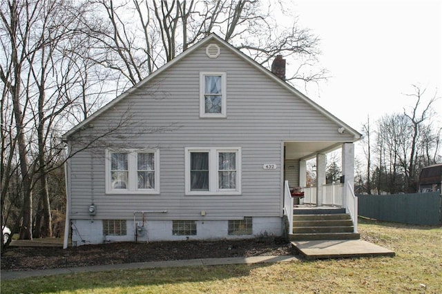 back of house with covered porch, a yard, a chimney, and fence