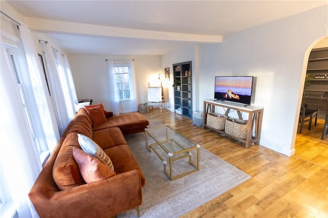 living area featuring arched walkways, beam ceiling, baseboards, and wood finished floors