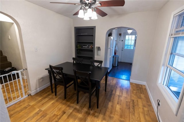 dining area with arched walkways, built in shelves, wood finished floors, a ceiling fan, and baseboards