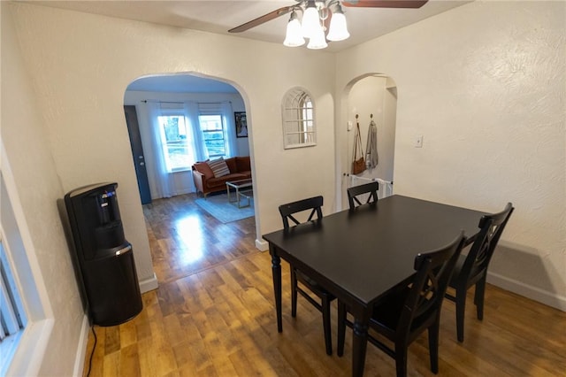 dining space featuring arched walkways, ceiling fan, baseboards, and wood finished floors