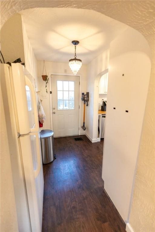 doorway featuring arched walkways, dark wood-style flooring, and baseboards