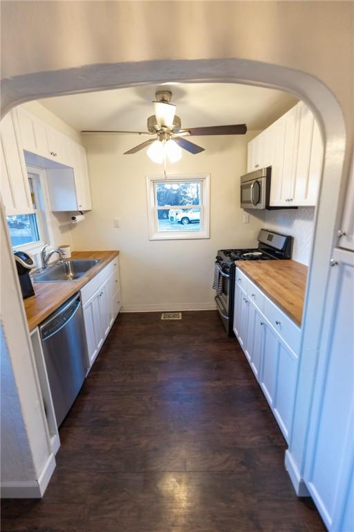 kitchen featuring arched walkways, stainless steel appliances, white cabinets, a sink, and wood counters