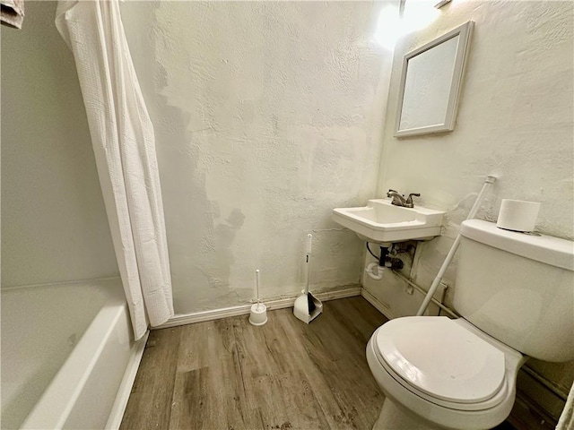 bathroom with a textured wall, toilet, wood finished floors, shower / bath combination with curtain, and a sink