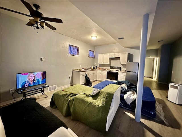 bedroom featuring freestanding refrigerator, visible vents, baseboards, and wood finished floors