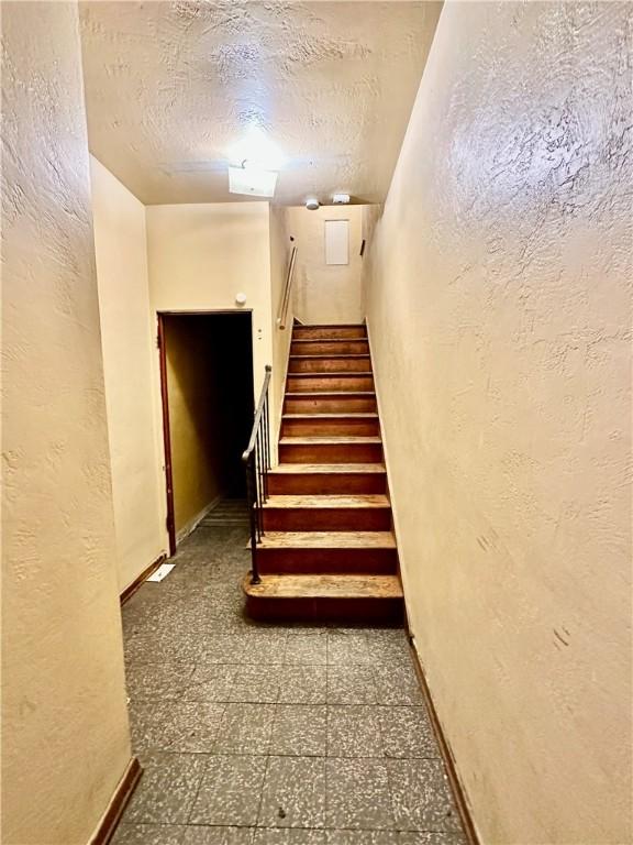 stairway featuring a textured ceiling, a textured wall, and tile patterned floors