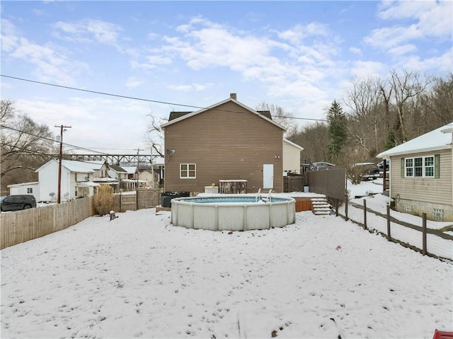 snow covered back of property with a wooden deck, fence, and a fenced in pool