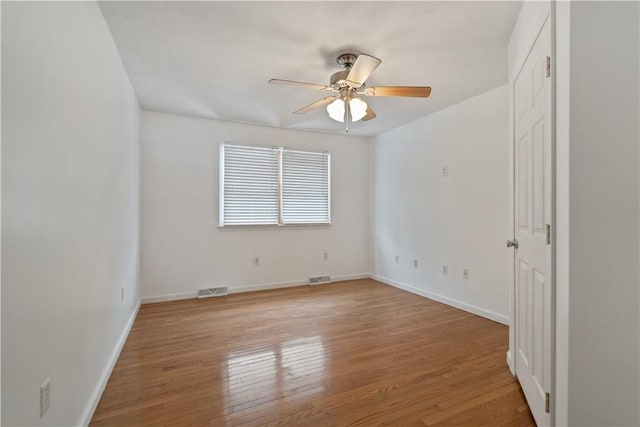 empty room featuring hardwood / wood-style floors, a ceiling fan, visible vents, and baseboards