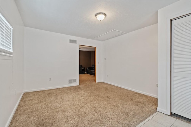 spare room with attic access, visible vents, baseboards, and light colored carpet