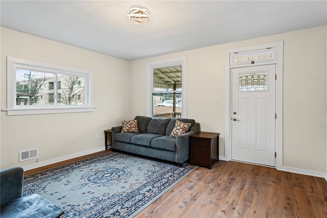 living area with a wealth of natural light, hardwood / wood-style flooring, visible vents, and baseboards