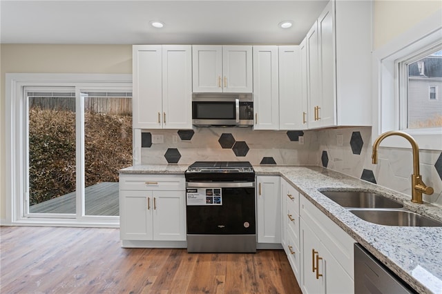 kitchen with wood finished floors, a sink, stainless steel appliances, white cabinetry, and backsplash