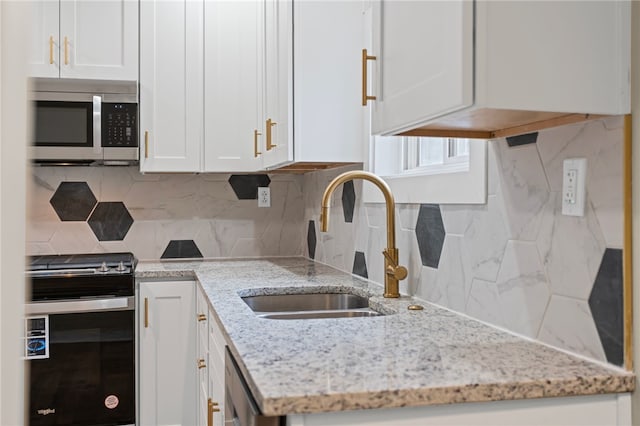 kitchen featuring stainless steel microwave, decorative backsplash, white cabinetry, a sink, and range