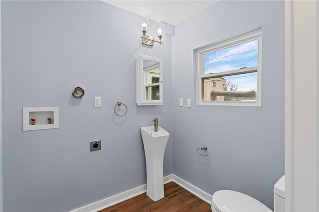 half bathroom with a notable chandelier, toilet, a sink, wood finished floors, and baseboards