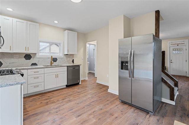 kitchen featuring backsplash, light wood-style flooring, appliances with stainless steel finishes, white cabinets, and a sink