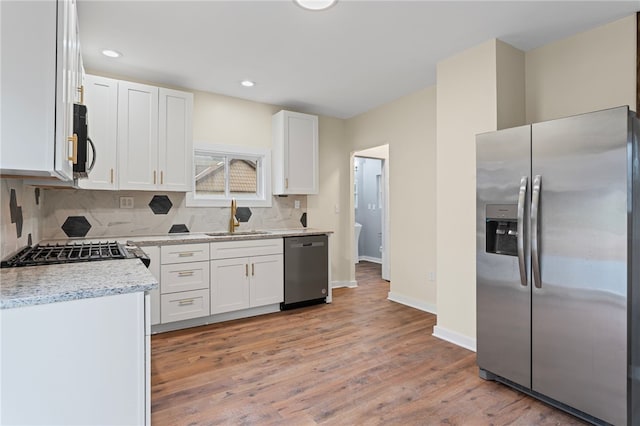 kitchen with light wood finished floors, white cabinets, appliances with stainless steel finishes, a sink, and backsplash