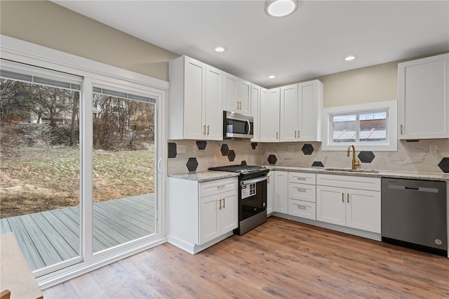 kitchen with stainless steel appliances, decorative backsplash, white cabinets, a sink, and wood finished floors