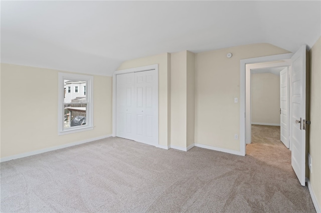 unfurnished bedroom with carpet floors, baseboards, a closet, and lofted ceiling