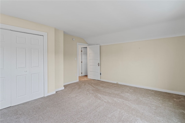 unfurnished bedroom featuring lofted ceiling, baseboards, a closet, and light colored carpet