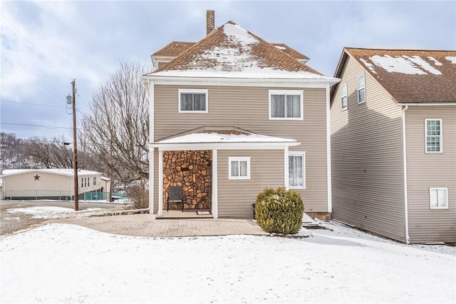 snow covered rear of property featuring a chimney