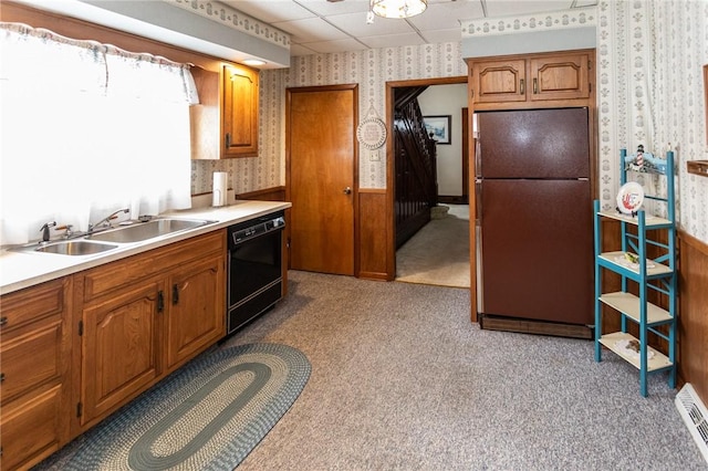 kitchen featuring wallpapered walls, a wainscoted wall, brown cabinets, black appliances, and a sink