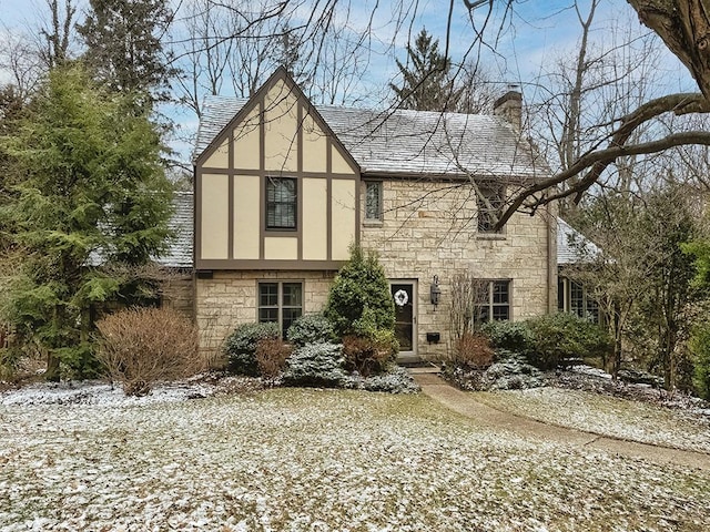 tudor home with stone siding, a chimney, roof with shingles, and stucco siding