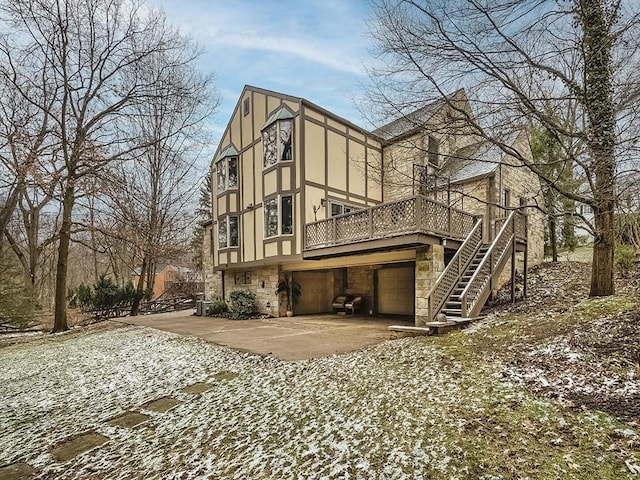 rear view of house featuring stairs, stone siding, concrete driveway, and stucco siding